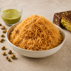 Bowl of roasted kataifi pastry with crispy golden texture beside pistachio chocolate pieces on a soft beige background.